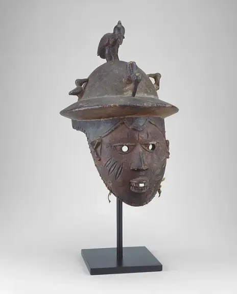 Carved wooden Egungun mask with a pith helmet and bird ornaments.