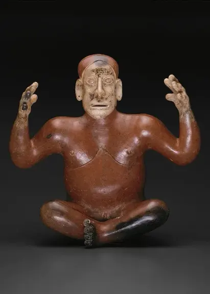 Seated red ceramic figure with both hands raised.