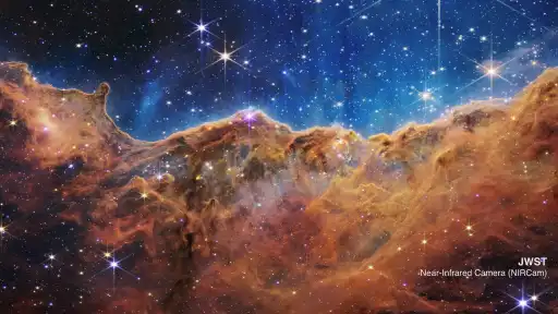Golden clouds of the Cosmic Cliffs beneath a field of blue and white stars