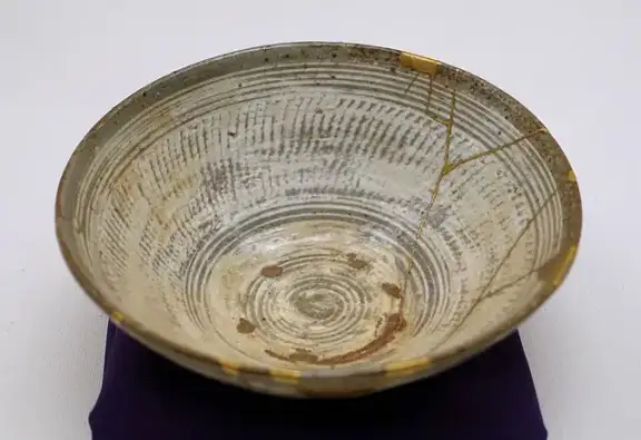 A Korean ceramic tea bowl repaired with visible gold lacquer using kintsugi.
