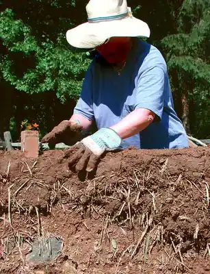 Cob (material): Woman constructs a wall out of Cob, a building material consisting of clay, sand, straw, water, and earth.